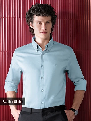 Mens Light Blue Satin Shirt, man sitting on a red leather couch in a stylish, dimly lit setting.