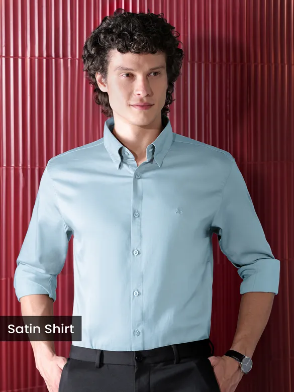 Mens Light Blue Satin Shirt, man sitting on a red leather couch in a stylish, dimly lit setting.