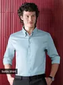 Mens Light Blue Satin Shirt, man sitting on a red leather couch in a stylish, dimly lit setting.