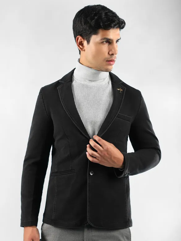 Man in a mens black blazer, with white turtleneck sweater, and grey trousers