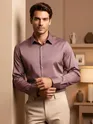 Man in a Mauve pink shining shirts with black trousers, posing against a red textured wall.