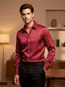 Mens red satin shirt, man sitting on a red leather couch in a stylish, dimly lit setting.